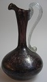 Italienischer 
Glaskrug, 20. 
Jahrhundert in 
bräunlichem 
Glas mit klarem 
Glasgriff. H.: 
14,5 cm.