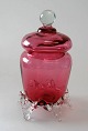 Jar in weinrot 
Glas, 20. 
Jahrhundert. 
Odense 
Glaswerke. 
F&uuml;&szlig;e 
und knopfh in 
Klarglas. ...