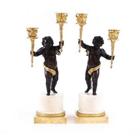 Et par lueforgyldte tidlig empire bronzekandelabre 
i form af to sortpatinerede putti bærende hver to 
lyseholdere i form af fakler stående på 
marmorbase. Frankrig ca. år 1795. H: 45cm