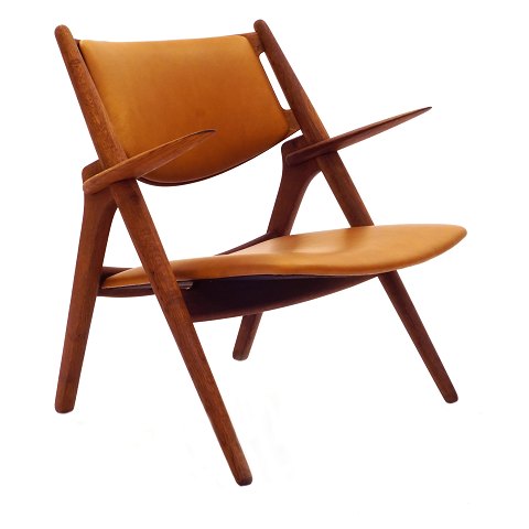 Hans Wegner Savbukkestol CH28. Hans J. Wegner, 
1914-2007, Savbukkestol med armlæn i patineret eg 
med cognac farvet læder. Fremstår i flot stand, 
nypolstret, med anilinlæder.