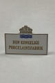 Royal 
Copenhagen 
Forhandler 
Skilt med guld
Måler 9,3cm x 
6,5cm
Har afslag på 
bagsiden.