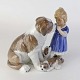 Figur i porcelæn med motiv af lille pige som klapper en Sankt Bernhard tæve, mens tævens hvalpe ...